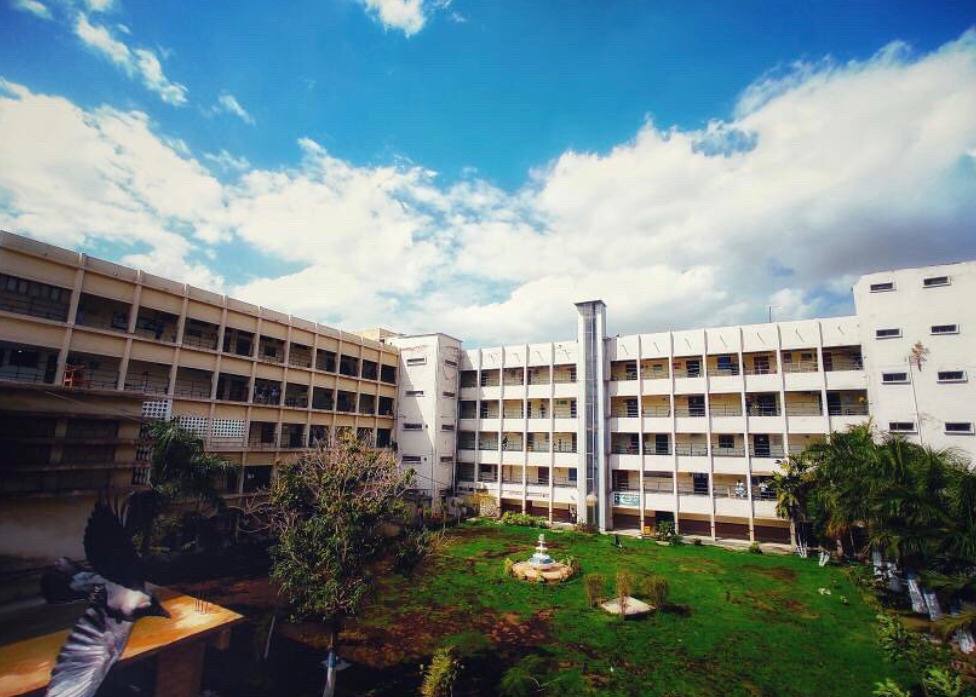 A large multi-story hostel building at Dawood University of Engineering and Technology in Karachi, with open balconies, a grassy courtyard, and a bright blue sky with scattered clouds.